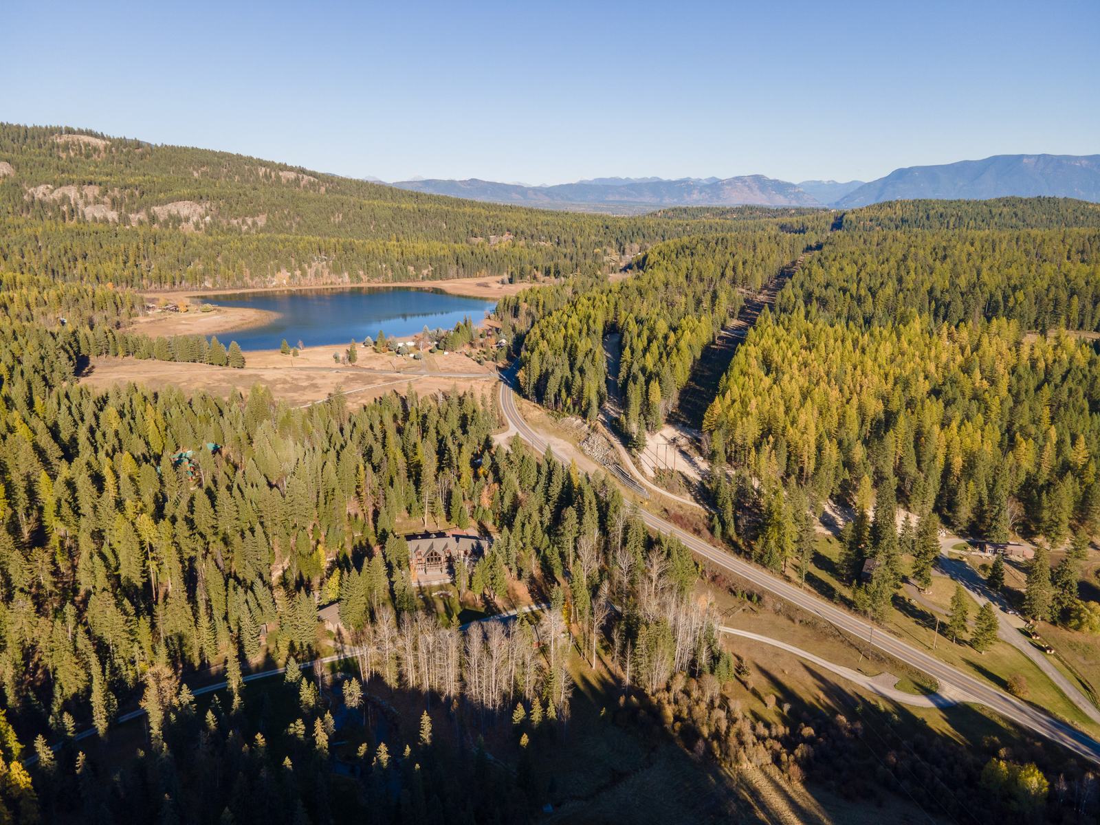 Aerial view over the forested hills around the property toward a lake and distant mountains