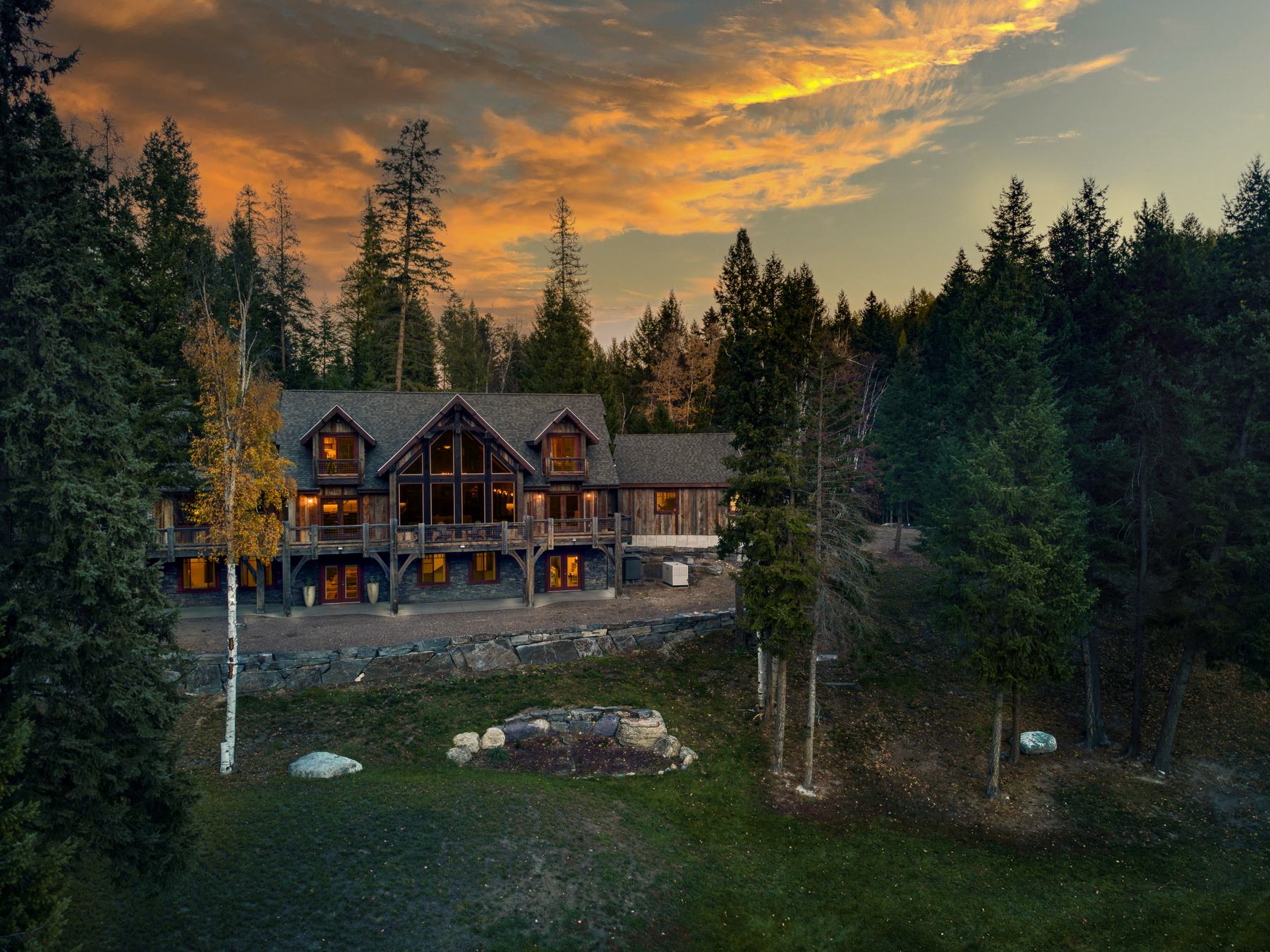 The Main House at Whitefish Outpost lit up at sunset, framed by tall pines and a birch