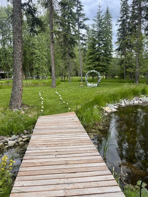 A wooden boardwalk crosses the pond to a ceremony arch of white flowers